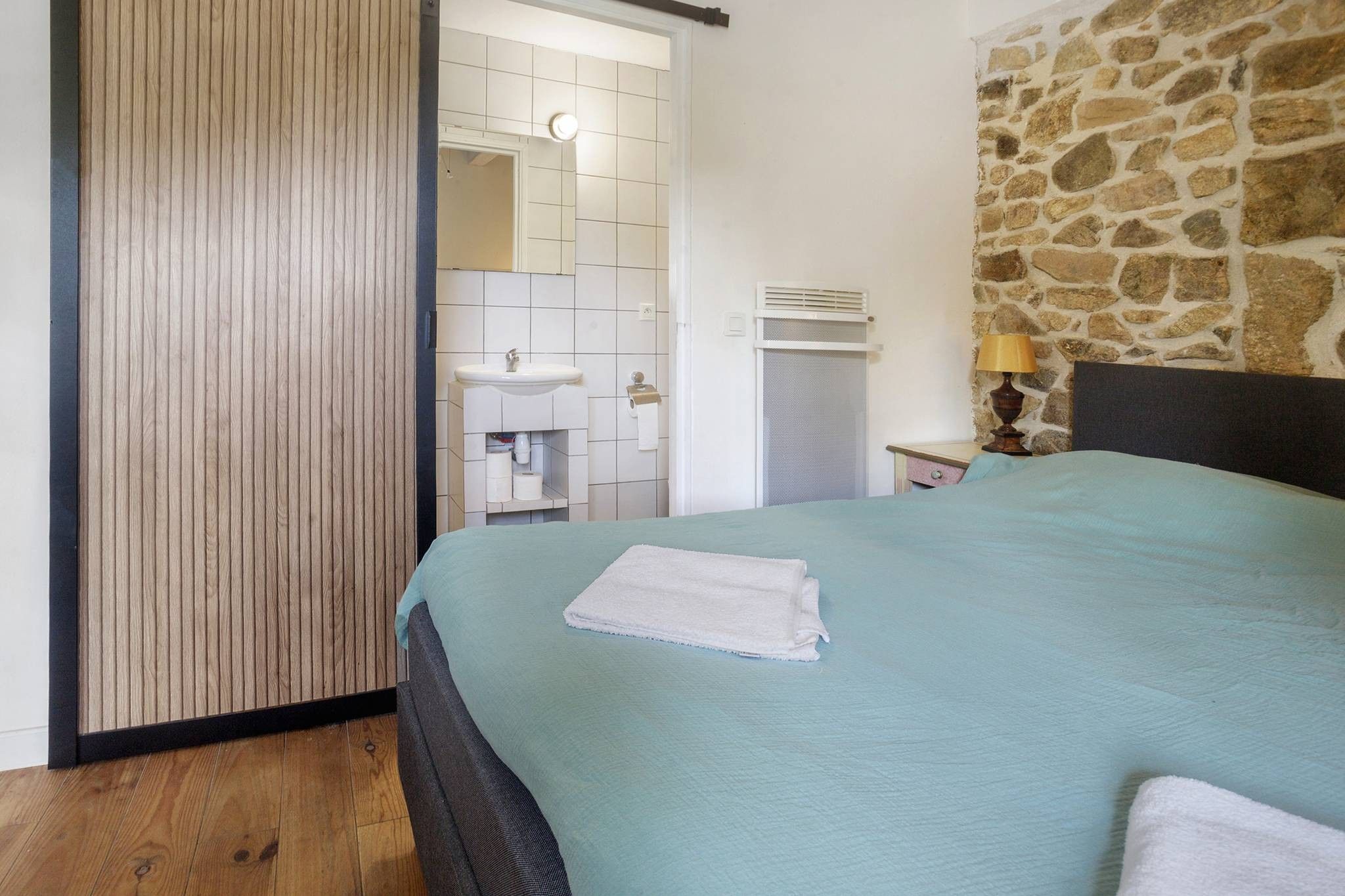 Un dormitorio con cama, un baño con lavamanos y una pared de piedra.