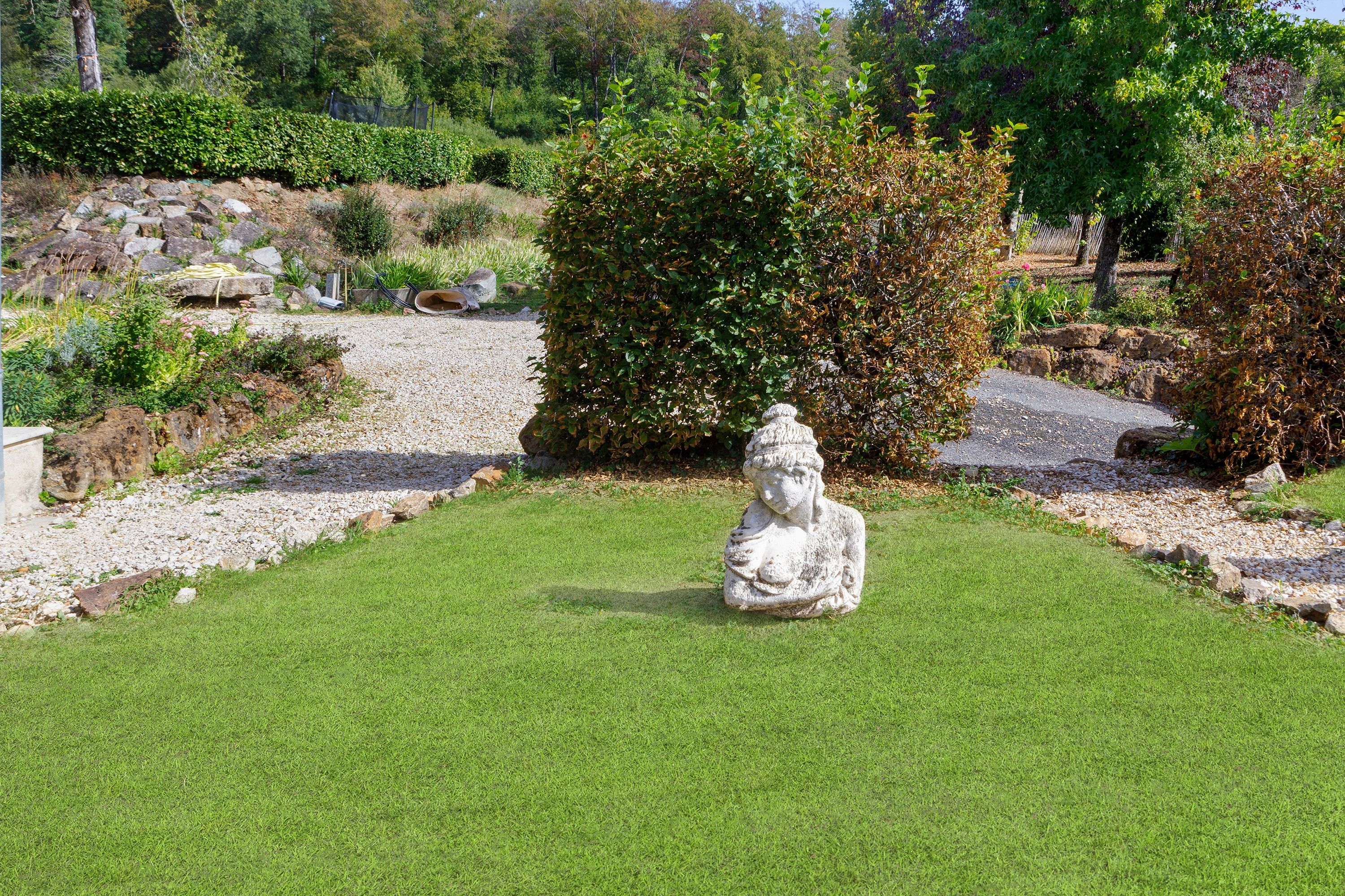 Un jardín con una estatua en el centro, rodeado de césped cuidado y diversas plantas.