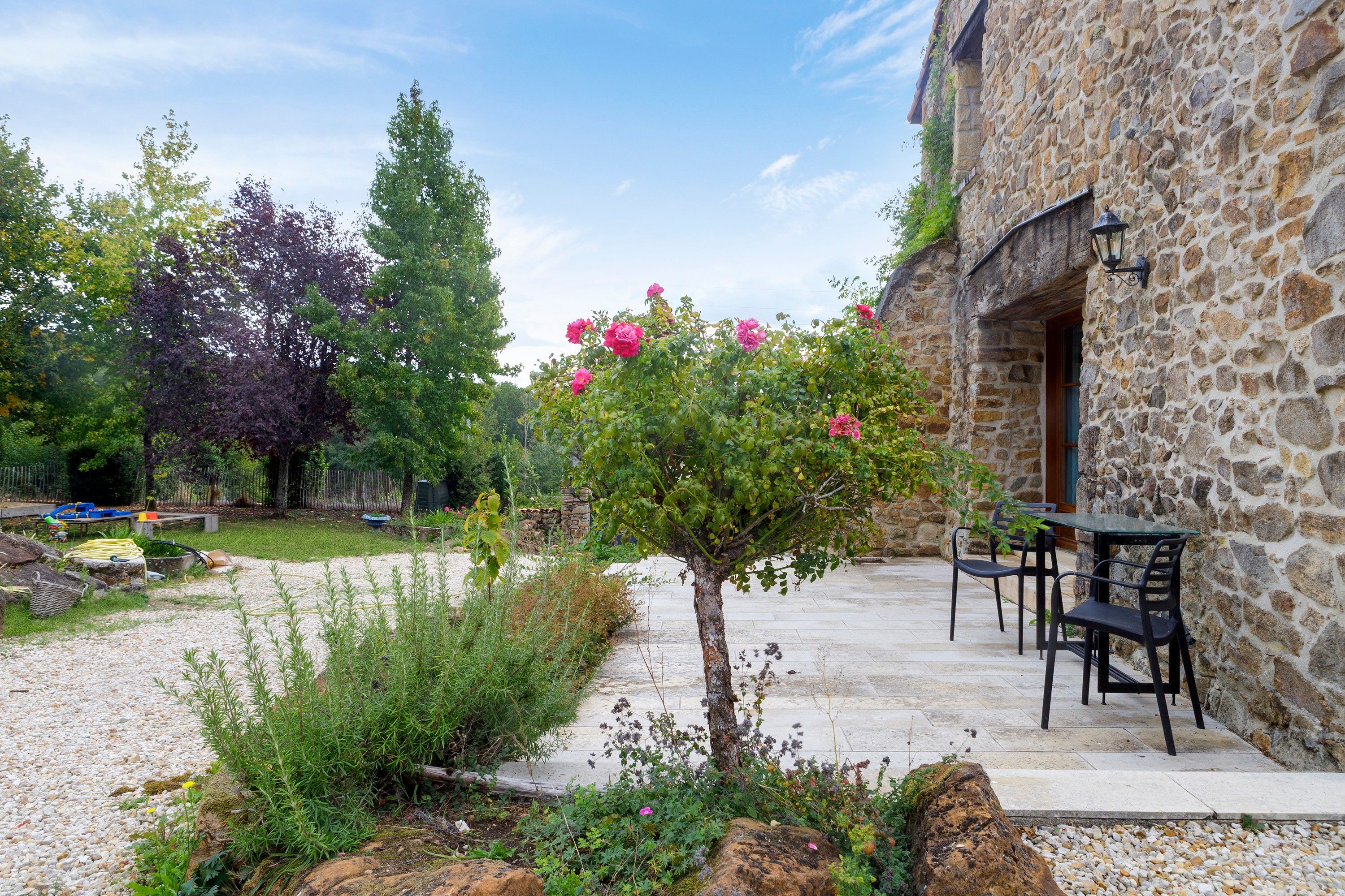 Un edificio de piedra con un patio, mobiliario exterior y un jardín lleno de plantas y flores.