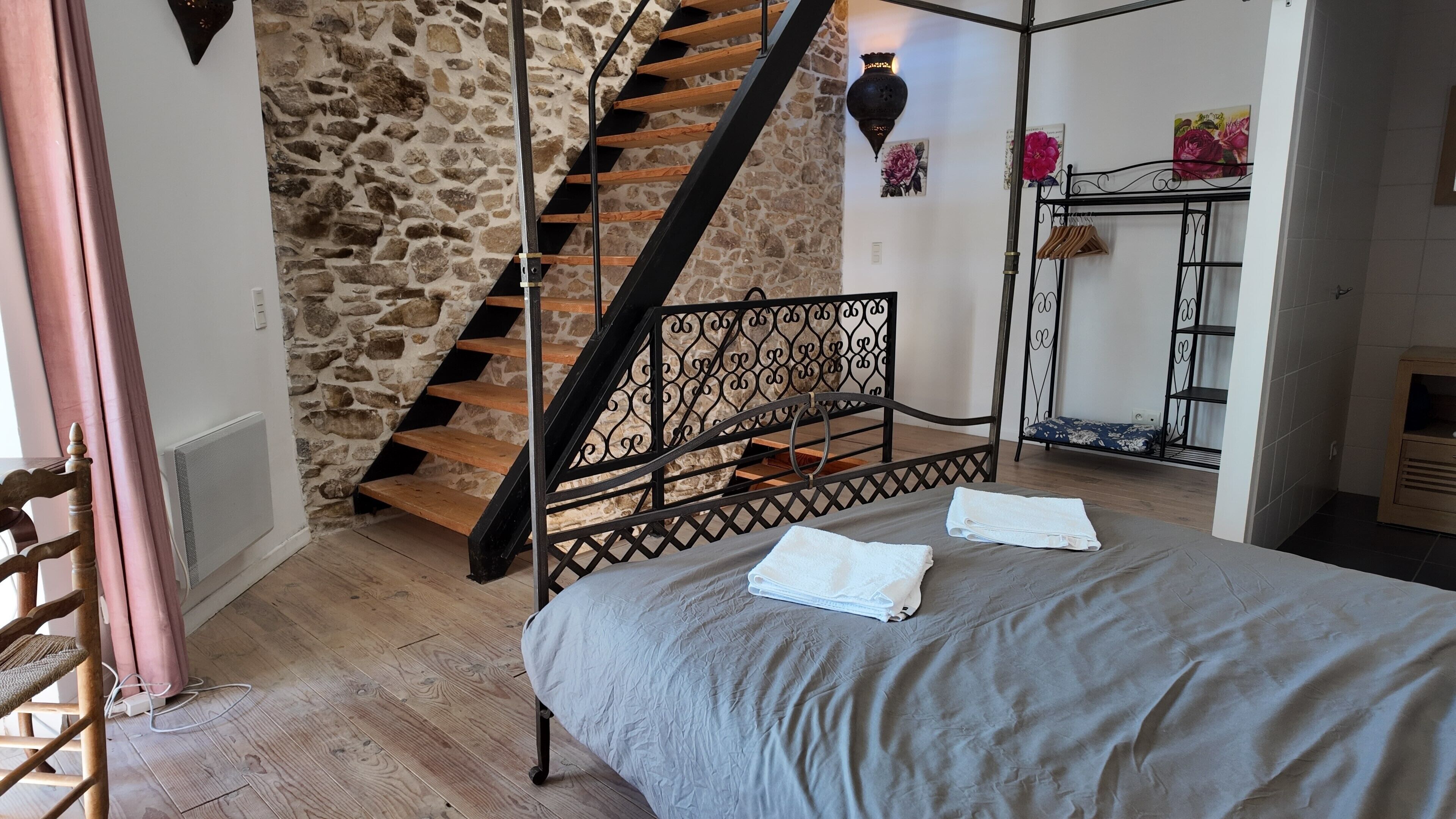 Ein Schlafzimmer mit Steinwand, einer Holztreppe, einem Bett mit grauer Bettdecke und einem Nachttisch mit Handtüchern.