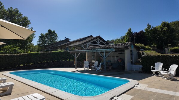 A swimming pool with lounge chairs, a covered patio, and a building with a tiled roof.
