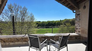 A balcony with a table and chairs, overlooking a green landscape and trees.