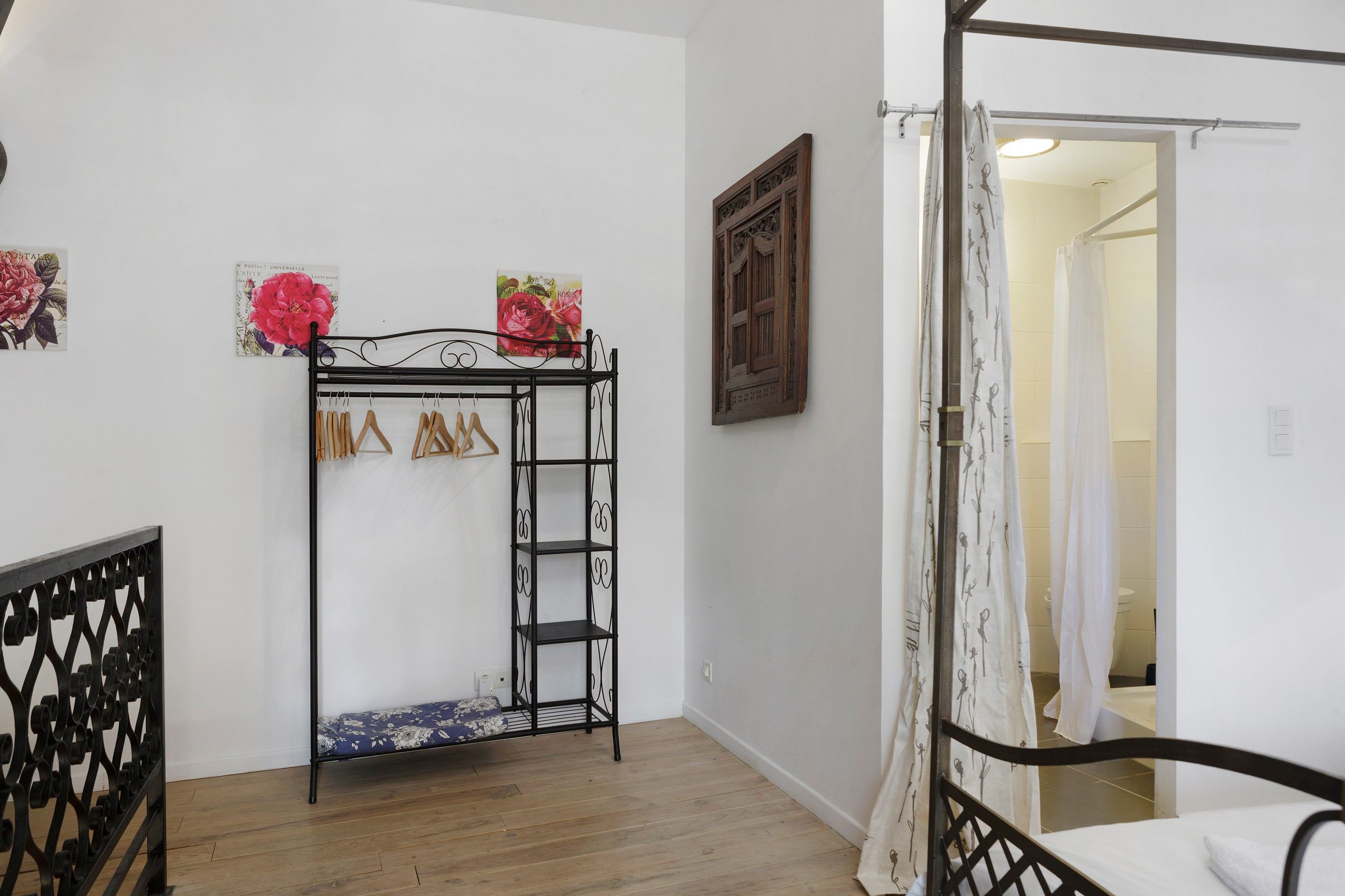 Une chambre avec un lit en métal, un plancher en bois, un mur blanc et une porte donnant sur une autre pièce.