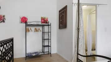Een slaapkamer met een metalen bedframe, een houten vloer, een witte muur en een deur naar een andere kamer.