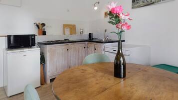 Een compacte keuken met witte apparaten, een houten eettafel en een vaas met bloemen.
