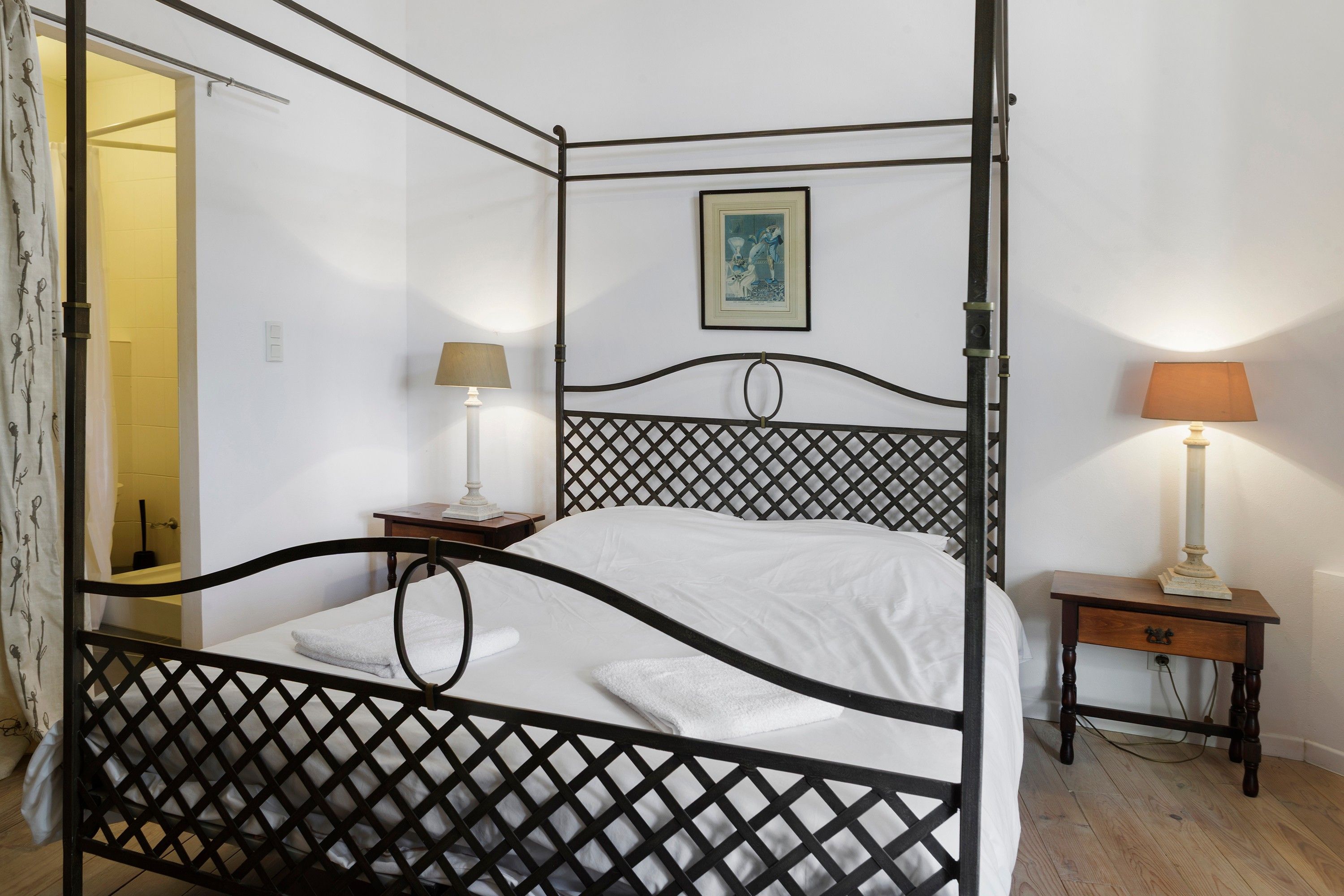 Un letto a baldacchino con decorazioni a griglia, un comodino con una lampada e un quadro incorniciato al muro.