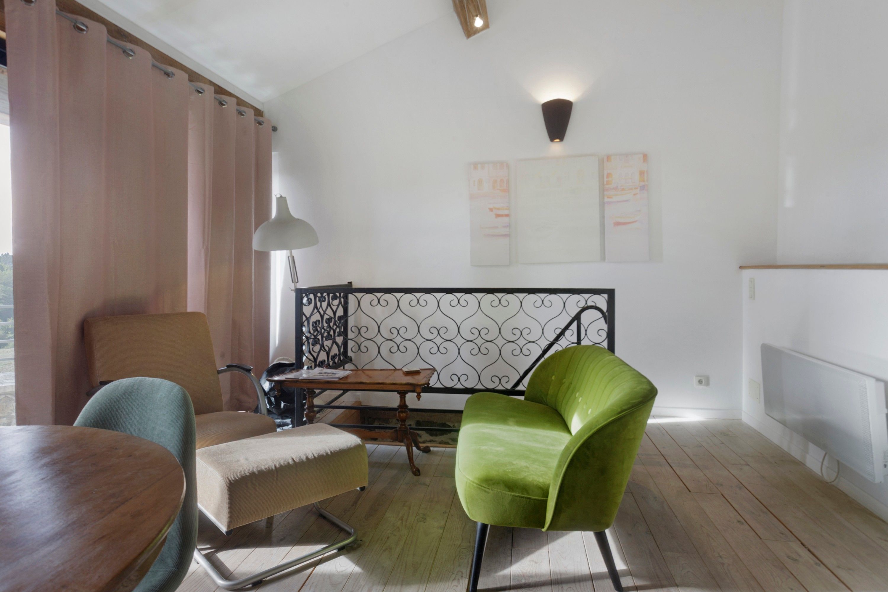 Une pièce comprenant une table à manger en bois, un fauteuil vert, un canapé, une lampe et une rambarde décorative en métal.