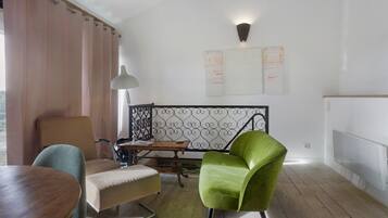 Quarto com mesa de jantar de madeira, poltrona verde, sofá, luminária e guarda-corpo metálico decorativo.
