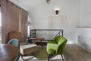 A room with a wooden dining table, a green armchair, a sofa, a lamp, and a decorative metal railing.