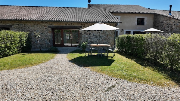 A stone building with a gravel driveway leading to a patio with a table and chairs.