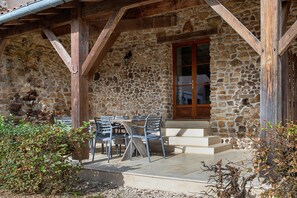 A stone building with a wooden porch, outdoor seating, and a door with glass panels.