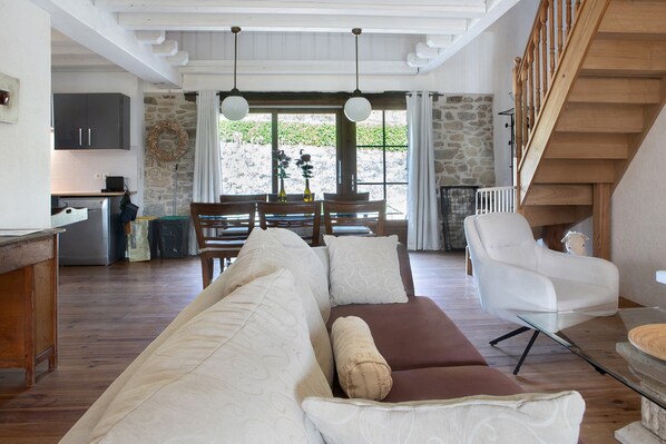 A spacious living area with a sofa set, a dining table, and a kitchen in the background.