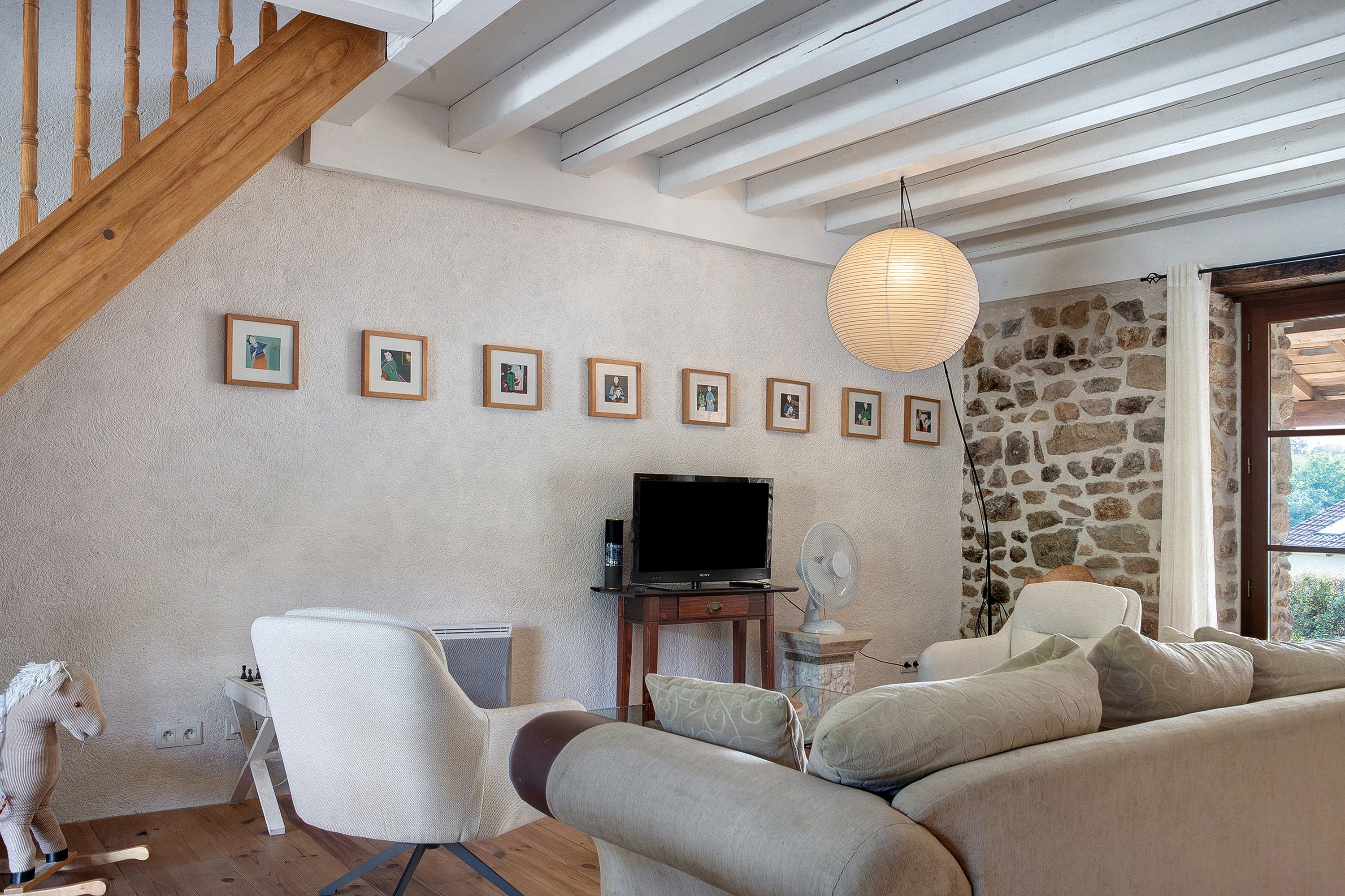Ein Wohnzimmer mit Steinwand, einer Holztreppe, einem Sofa, einem Fernseher und gerahmten Bildern an der Wand.