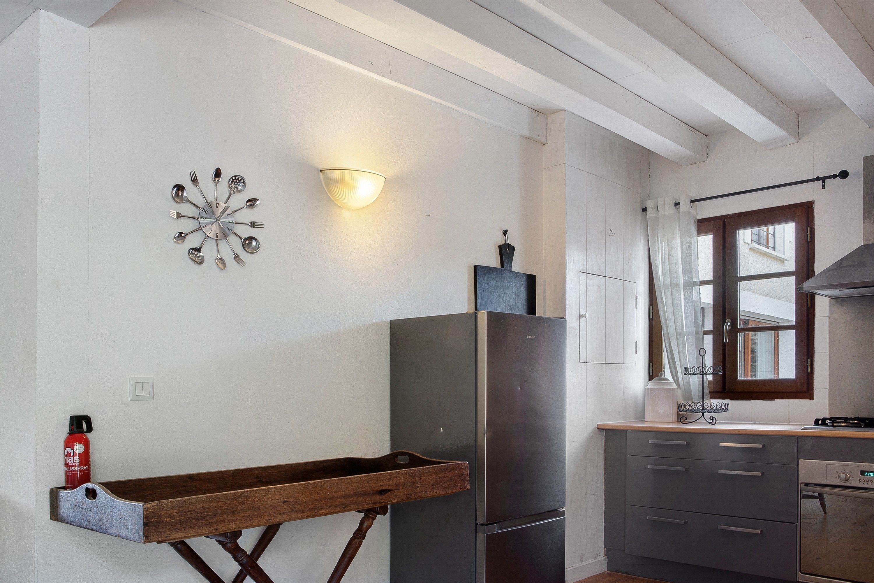 Een keuken met een houten droogrek, een roestvrijstalen koelkast en een wandlamp.