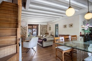 A spacious living area with a wooden staircase, a stone wall, and a dining area with a glass table.