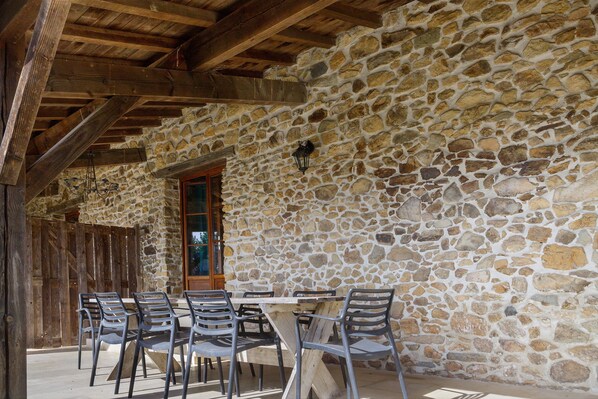 A stone-walled outdoor seating area with a wooden ceiling and a table with chairs.