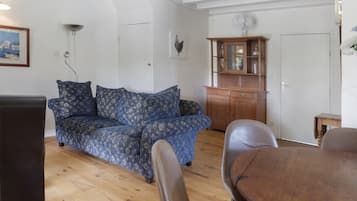 A living room with a blue patterned sofa, a wooden cabinet, and a dining table.