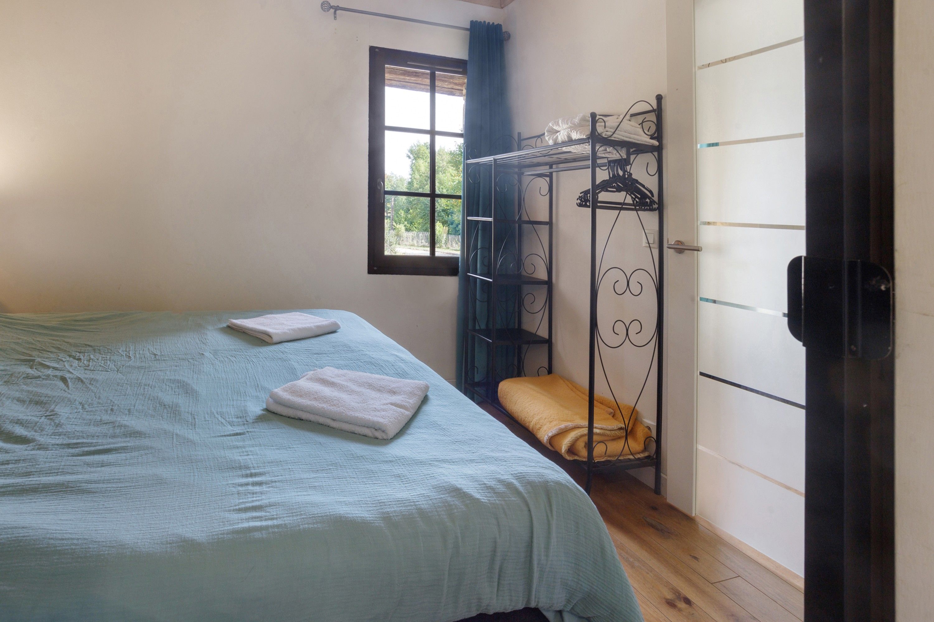Quarto com cama, janela, guarda-roupa e estrutura de metal com um banco.