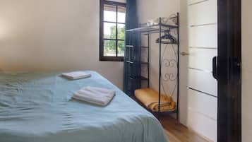 A bedroom with a bed, a window, a wardrobe, and a metal bed frame with a bench.