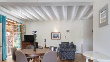 A dining area with a wooden table and chairs, a sofa, and a television on a stone wall.