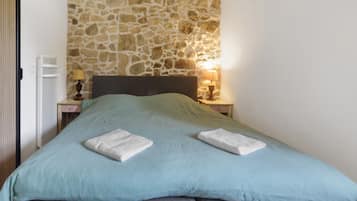 A bed with a stone wall backdrop, a bedside lamp, and a bedside table.