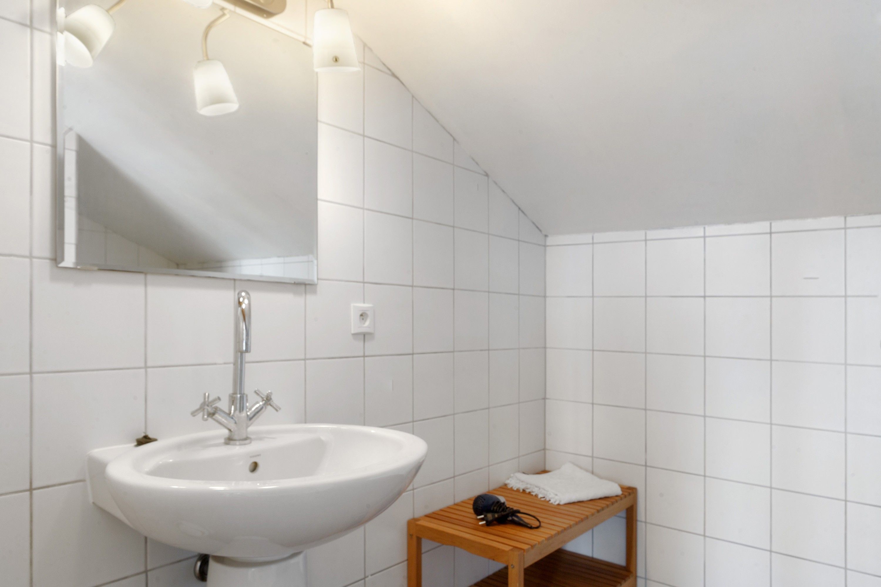 Un baño con un lavabo blanco, un espejo y un estante de madera con una toalla y un secador de pelo.