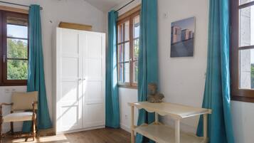 A room with a wooden floor, a white wardrobe, a wooden chair, a small table, and teal curtains.