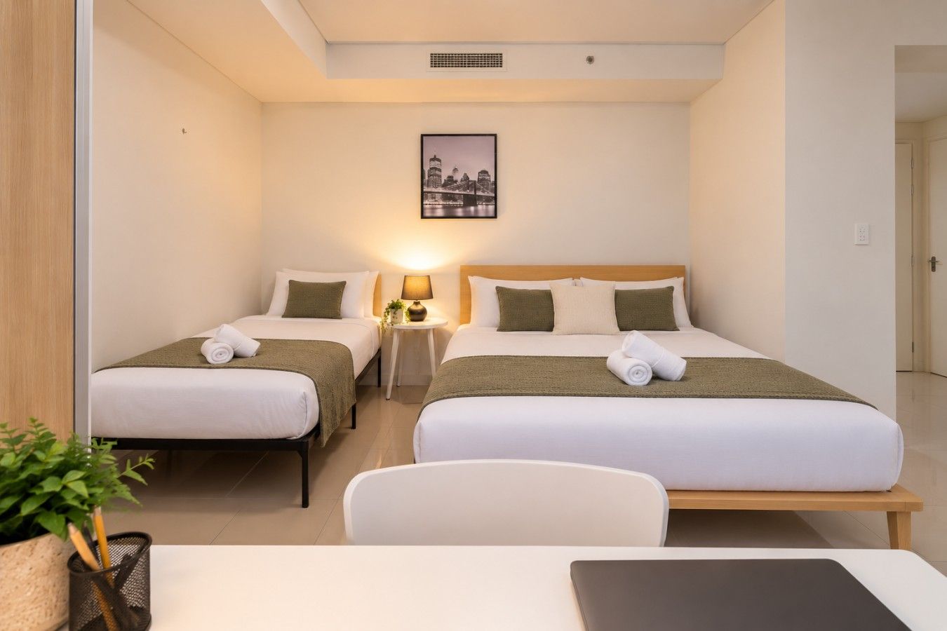 Ein Hotelzimmer mit zwei Betten, einem Schreibtisch, einem Stuhl, einer Lampe und einem gerahmten Bild an der Wand.