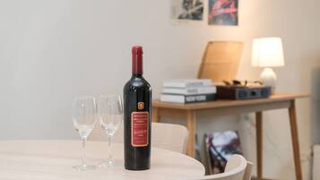 Une bouteille de vin sur une table, avec deux verres, une lampe et des livres en arrière-plan.