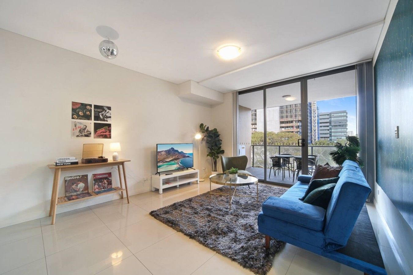 Ein modernes Wohnzimmer mit einem blauen Sofa, einem Flachbildfernseher, einem Couchtisch und einem großen Fenster mit Blick auf die Stadt.