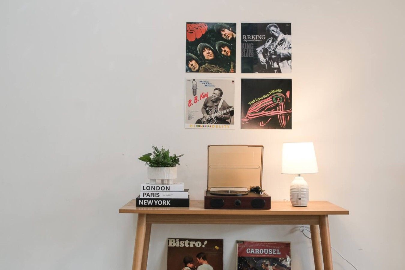 Eine Wand mit Postern, einer Pflanze, einer Lampe und einem Stapel Bücher mit Städtenamen.