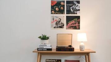 Eine Wand mit Postern, einer Pflanze, einer Lampe und einem Stapel Bücher mit Städtenamen.