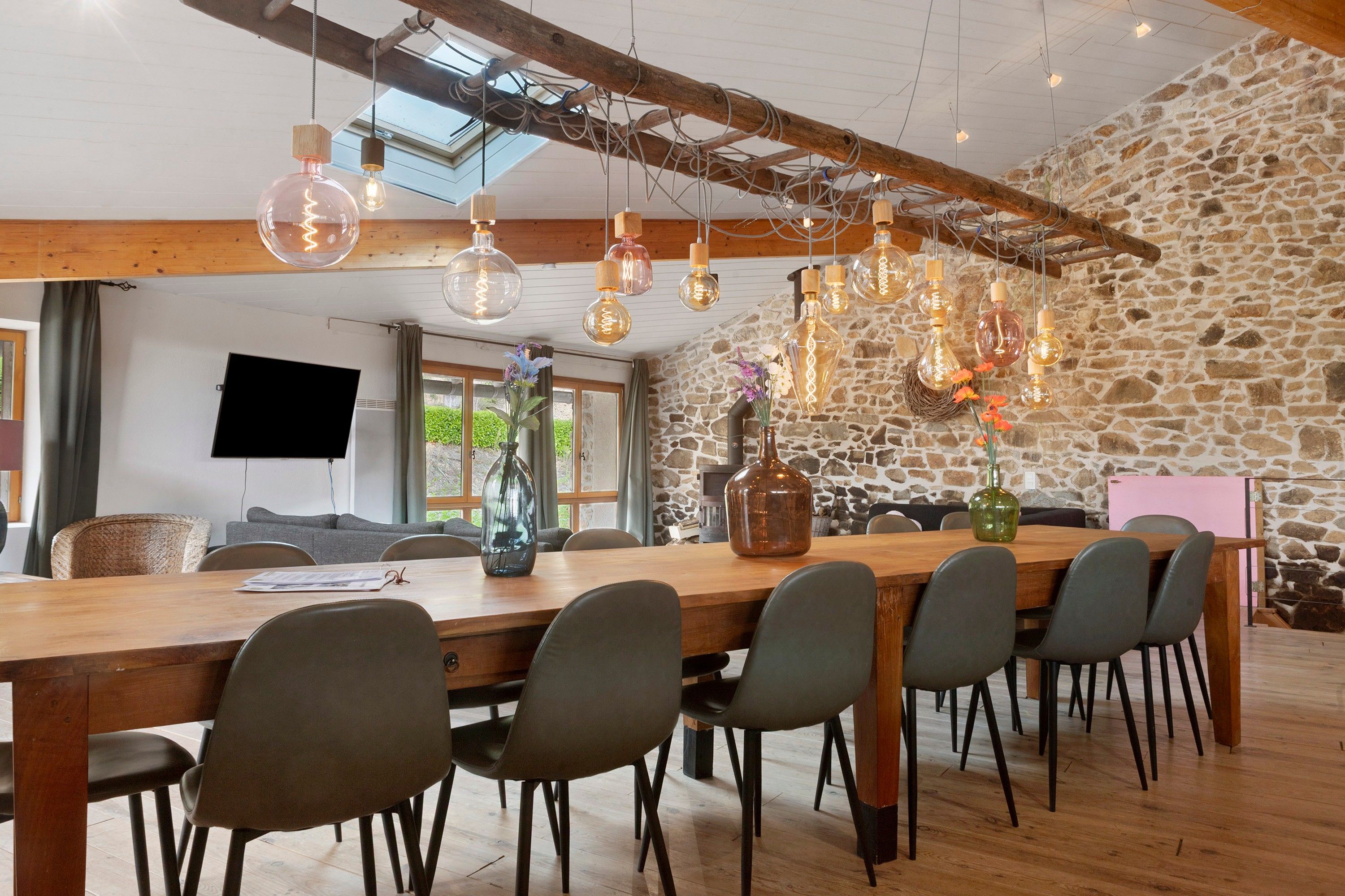 A spacious dining area with a long wooden table, multiple chairs, and hanging pendant lights.