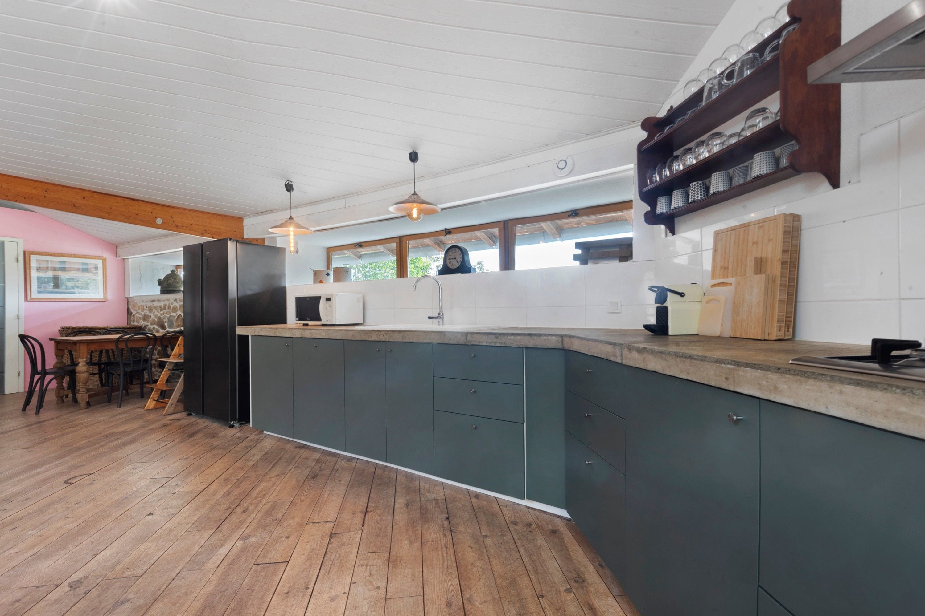 Une cuisine moderne avec un plancher en bois, un îlot central intégré doté d’un évier et une horloge au mur.