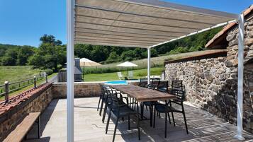 Eine Terrasse im Freien mit Tisch und Stühlen, einem Pool und einer Steinmauer.