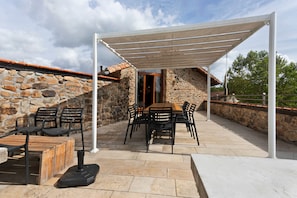 An outdoor patio with stone walls, a covered seating area, and a table with chairs.