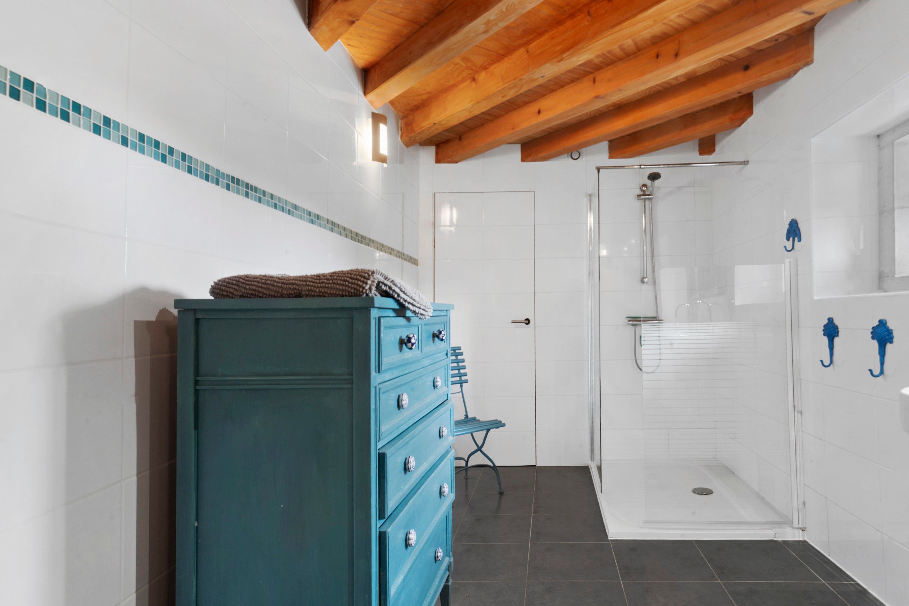 Ein Badezimmer mit Holzboden, einer blauen Kommode, einer Duschkabine mit Glastür und Fliesenboden.