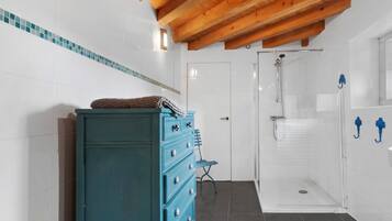Ein Badezimmer mit Holzboden, einer blauen Kommode, einer Duschkabine mit Glastür und Fliesenboden.