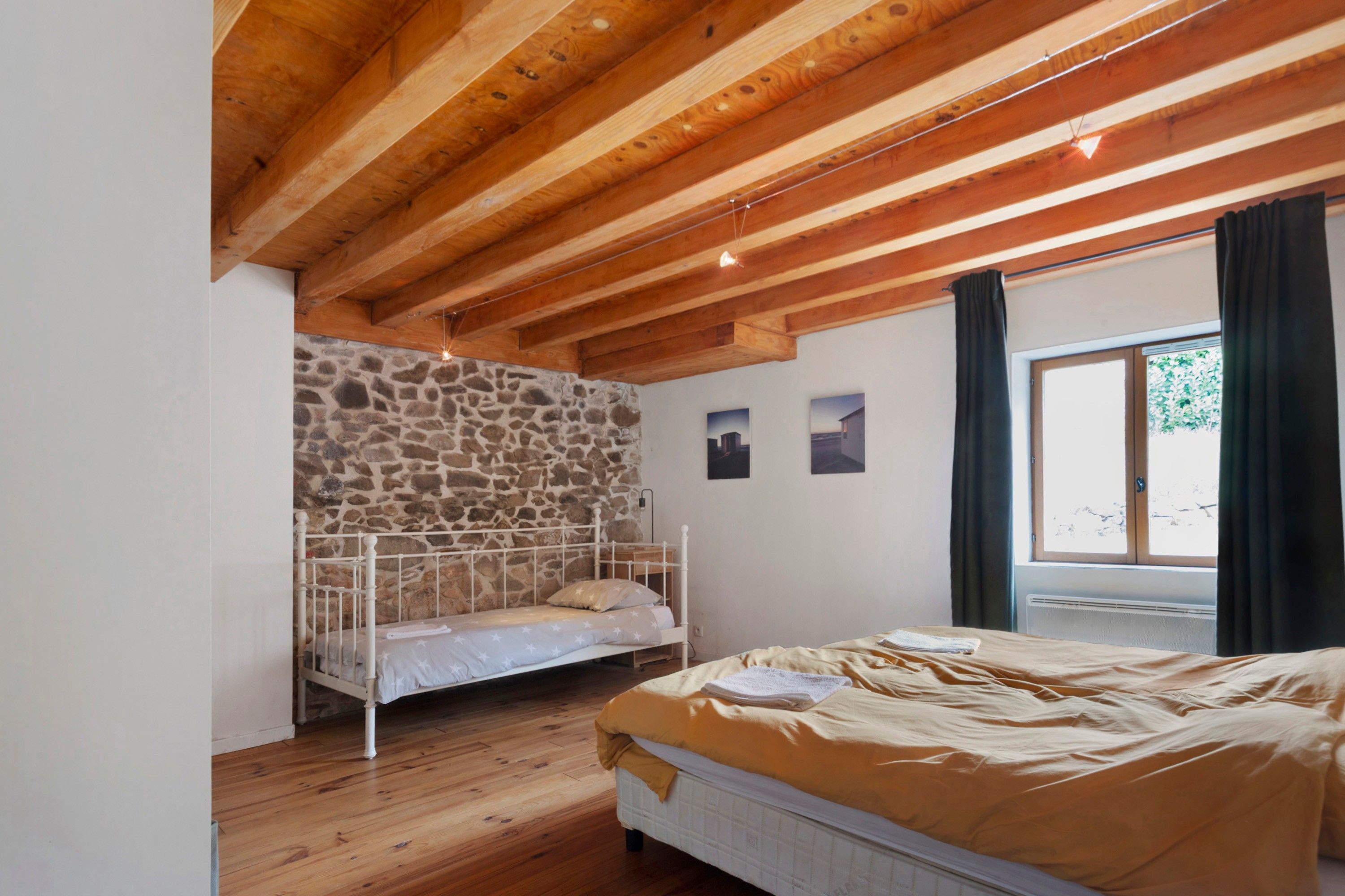 Un dormitorio con literas, pared de piedra, ventana con cortinas y techo de madera.