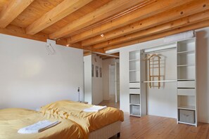 A bedroom with a wooden ceiling, a bed with yellow bedding, and a white wardrobe with multiple shelves.
