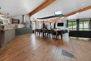 A spacious kitchen with a dining area, wooden flooring, and a large window providing natural light.