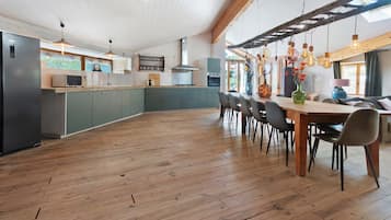 Cozinha ampla com piso de madeira, área de refeições com mesa e cadeiras de madeira, e vista para o exterior por grandes janelas.