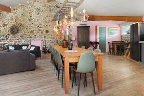 A dining area with a wooden table and chairs, a stone wall, and a kitchen in the background.