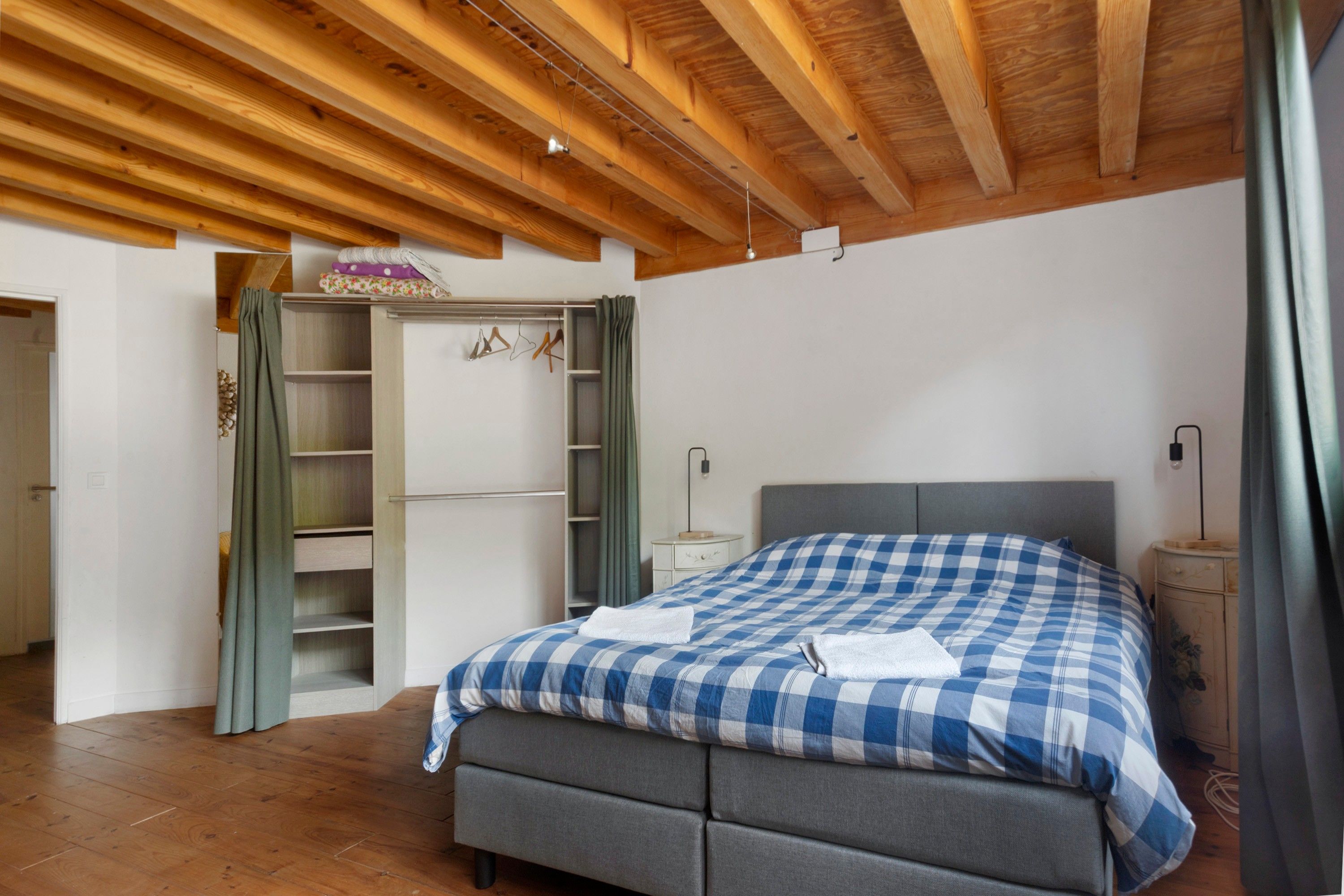 A bedroom with a bed, a wardrobe, and a ceiling with wooden beams.