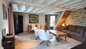 A spacious living area with a wooden floor, a stone wall, a staircase, and a dining set.