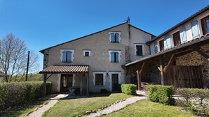 A two-story house with a covered patio, stone walls, and a gravel pathway.