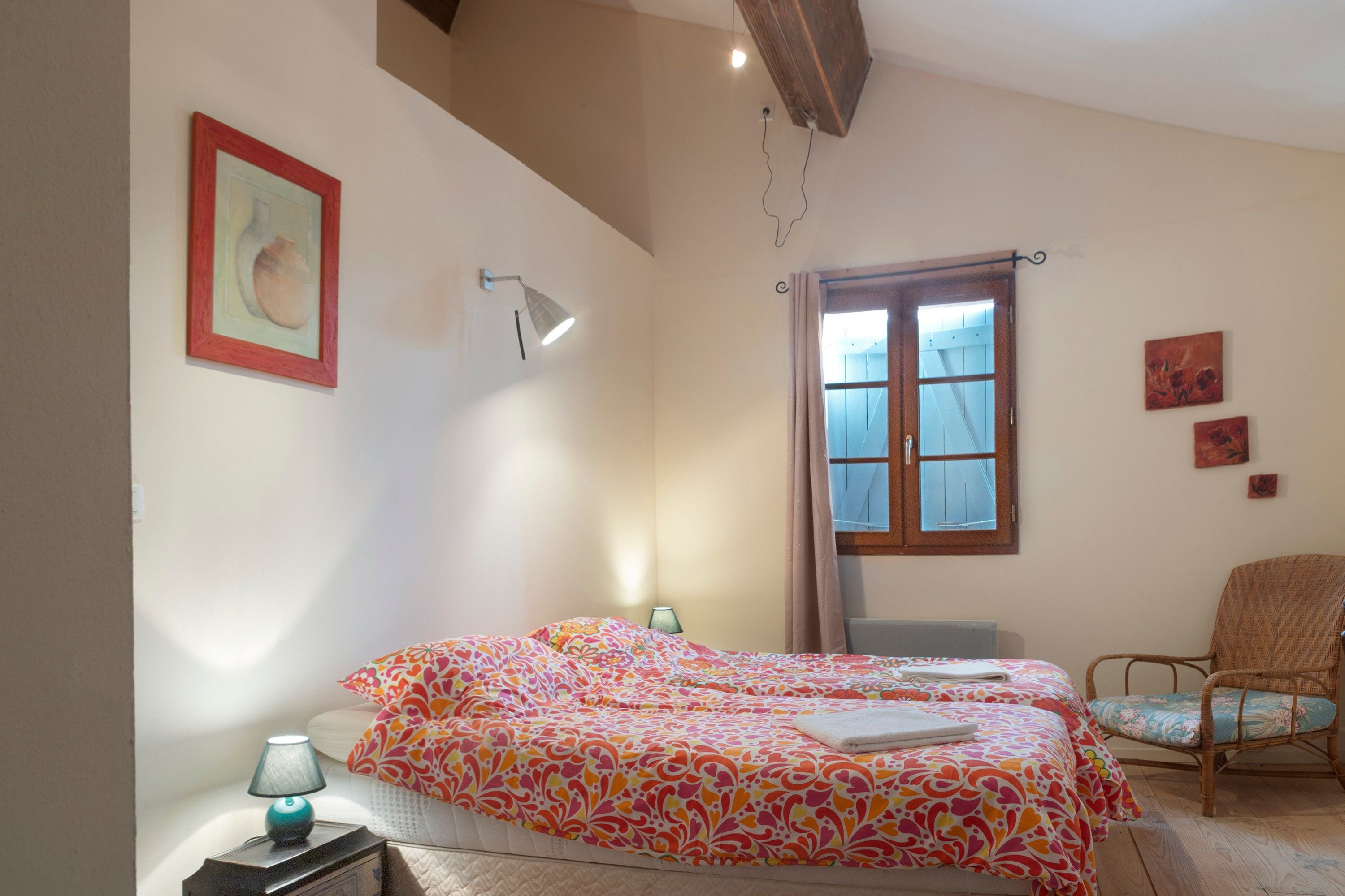 A bedroom with a bed, a chair, a desk, a lamp, a window with curtains, and a painting on the wall.