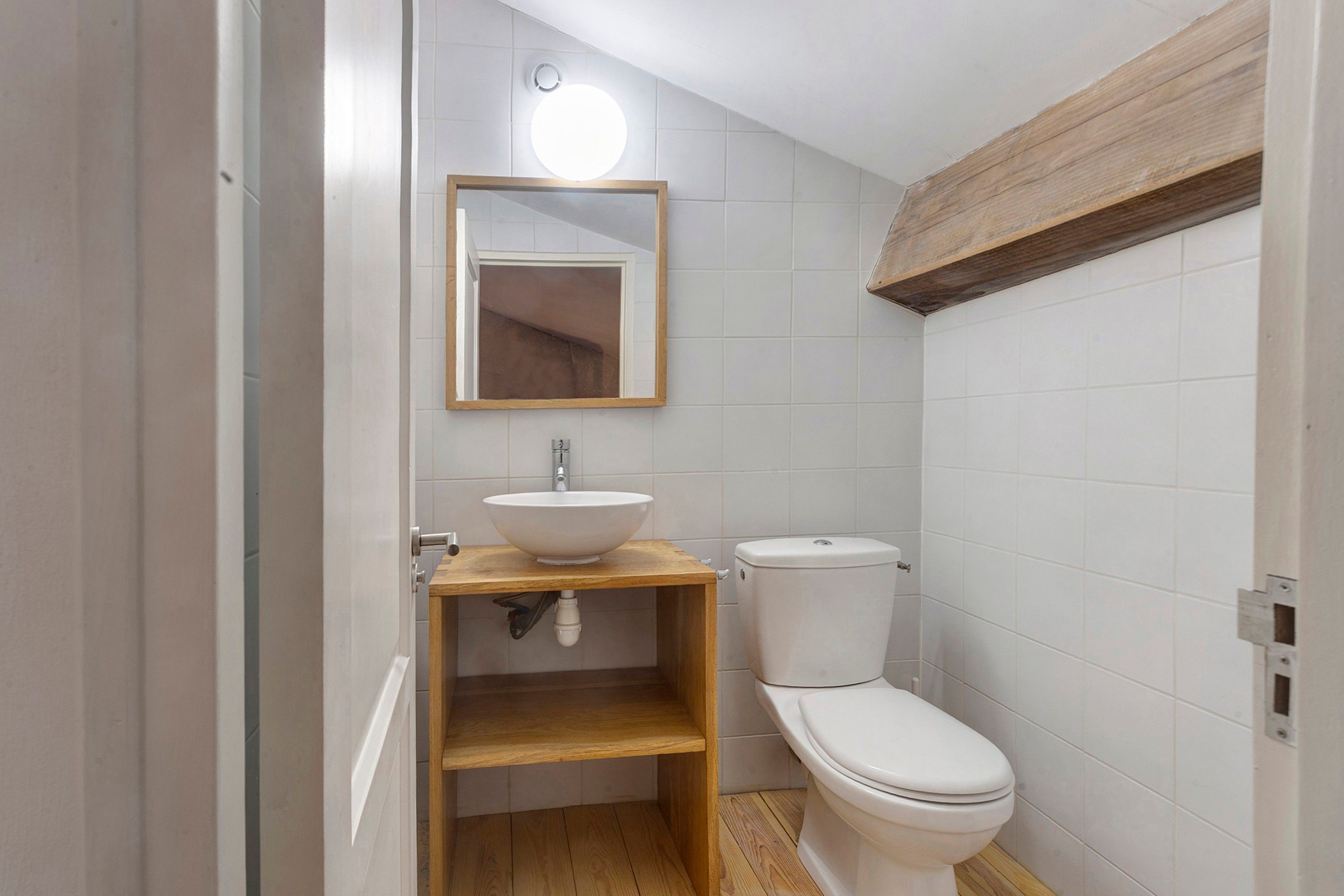 Een badkamer met een houten wastafelmeubel, een witte wasbak, een toilet en een spiegel met een lamp erboven.