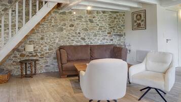 Un salon chaleureux avec un mur en pierre, un canapé en cuir marron, un fauteuil blanc et une table basse en bois.