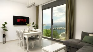 Moderni olohuone, jossa on ruokailutila, seinälle asennettu taulutelevisio ja suuri ikkuna, josta avautuu näkymä merelle.
